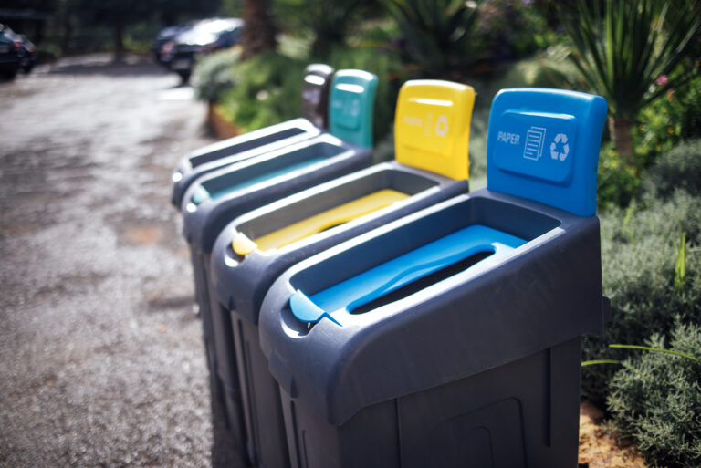 Outdoor recycling bins in vibrant colors, designed for waste separation, placed in a landscaped area, encouraging eco-friendly practices and community involvement