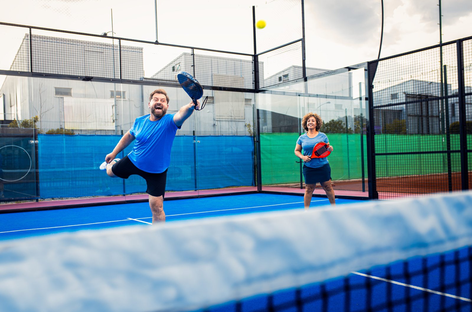 Mixed adult couple palying padel on outdoor court.