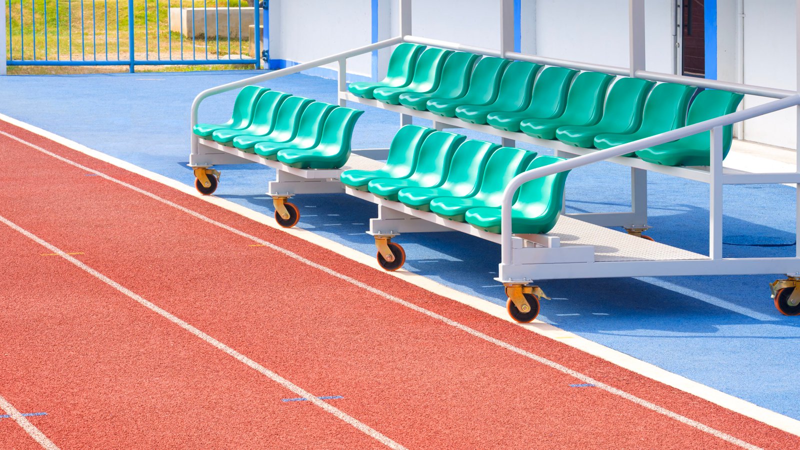 Reserve and coaching staff bench on rubber floor with red synthetic running tracks in outdoor soccer stadium, perspective side view with copy space