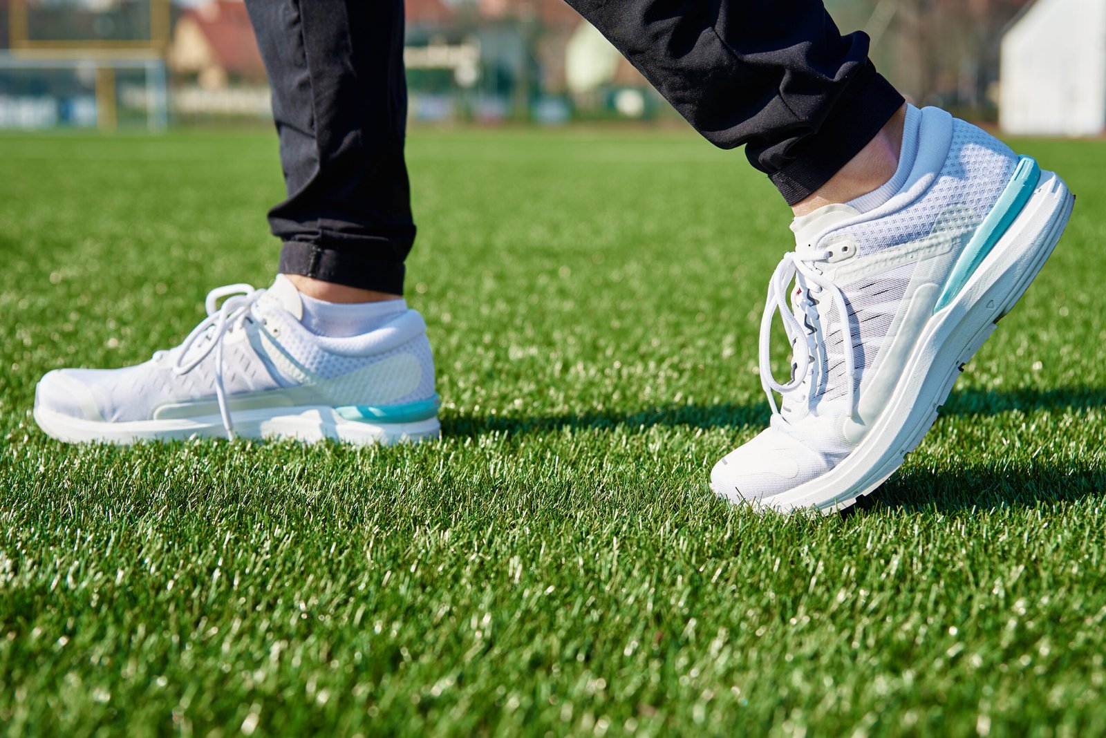 Male runner feet with white sneakers at stadium with green grass, close up. Sport sneakers for jogging. Fitness and healthy lifestyle concept