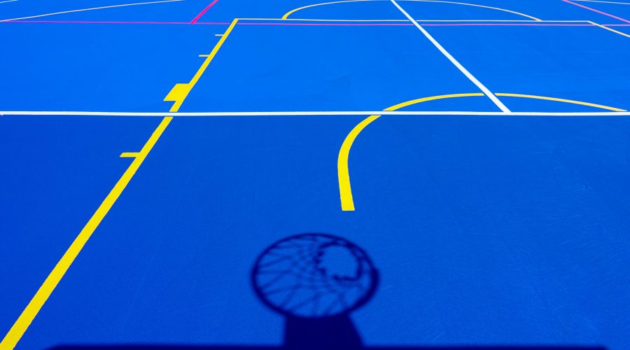 Shadow of a basketball basket on the floor of the court, painted blue and background with lines.