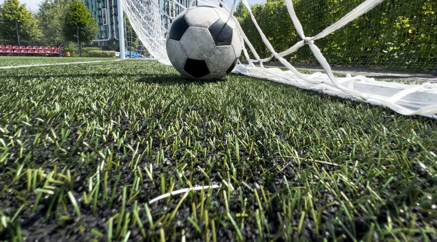 Soccer football in Goal net with green grass field. For sport concept. High quality photo